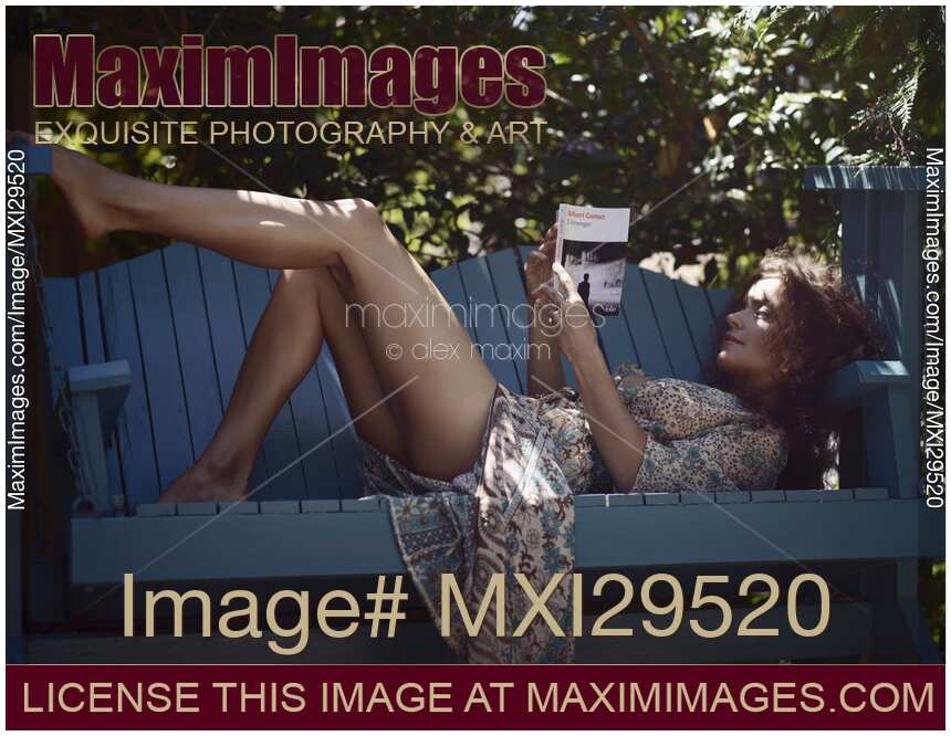 Sensual portrait of a woman reading a book lying on a garden bench