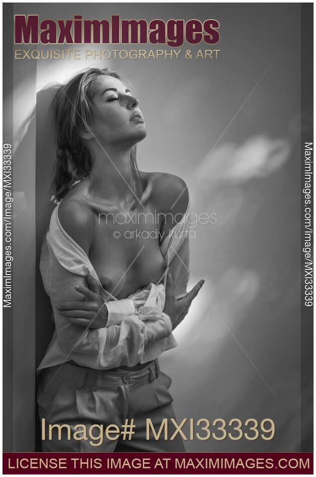 Sensual portrait of a woman standing topless leaning against a wall in open shirt with her breasts bared