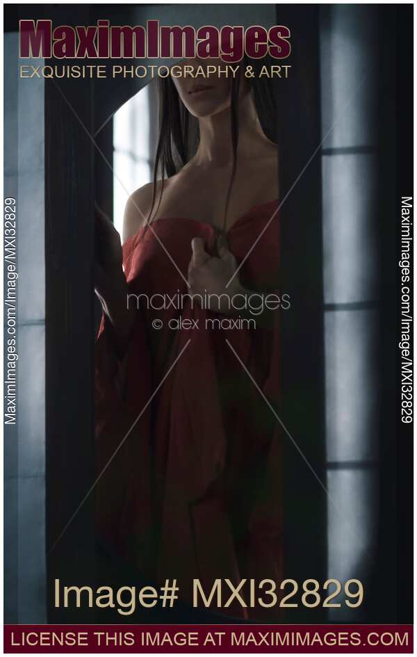 Sensual portrait of an Asian woman in undone red kimono standing by an open shoji window of a Japanese house