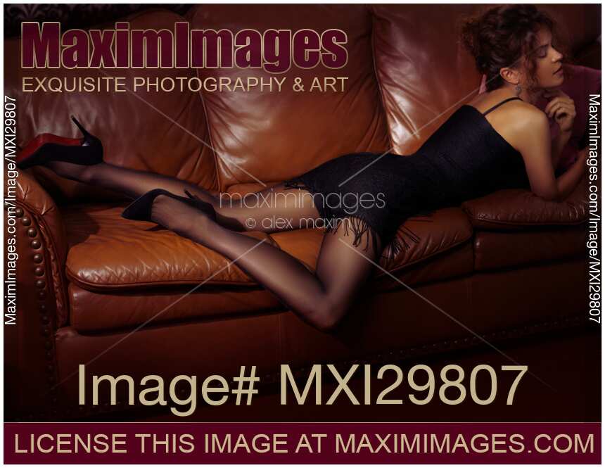 Sensual portrait of sexy woman lying on brown leather couch in black dress stockings and high heel shoes