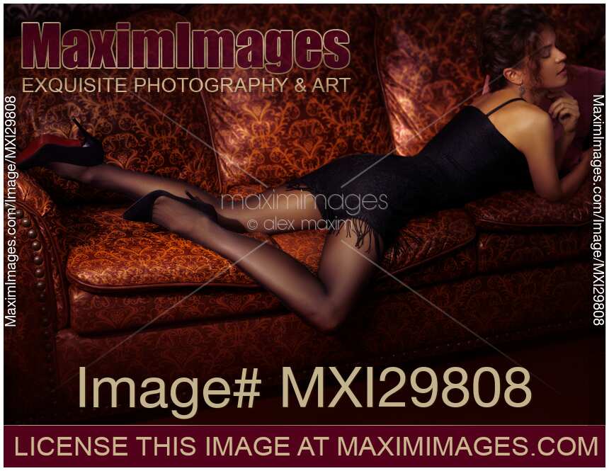 Sensual portrait of sexy woman lying on luxurious couch in black dress stockings and high heel shoes