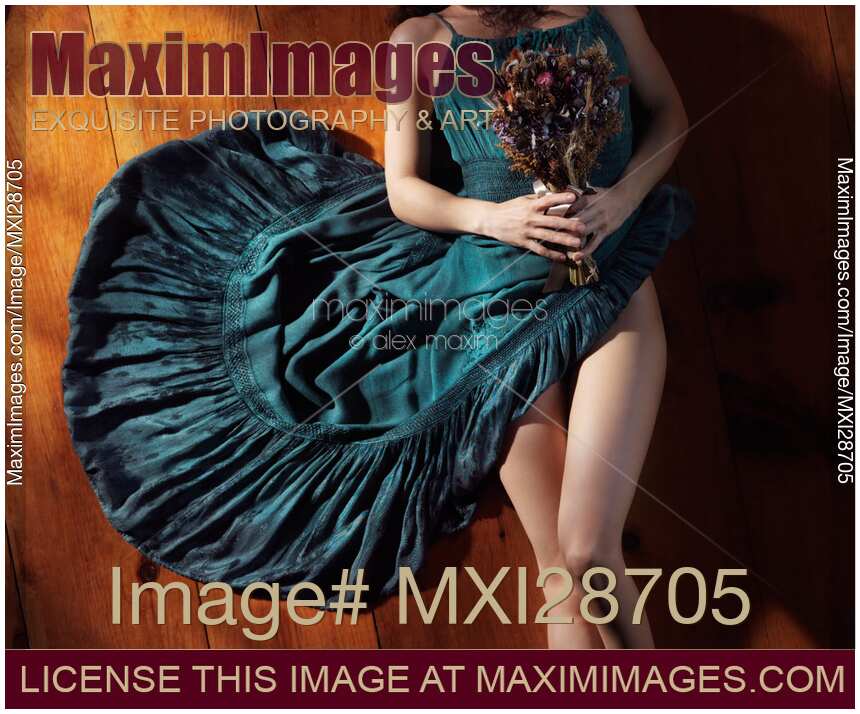 Sensual portrait of woman in blue dress with bare legs holding flowers lying on the floor