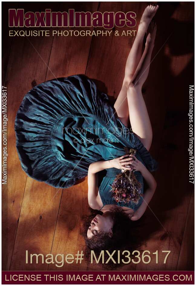 Sensual portrait of woman in green dress with bare legs lying on the floor holding flowers