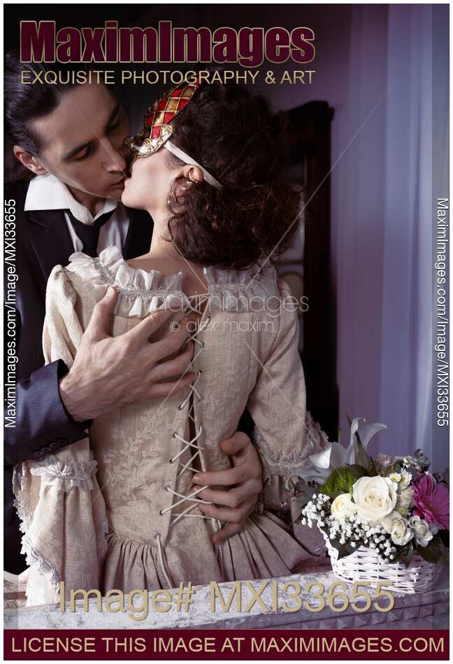 Sensual romantic portrait of a kissing couple. Elegant man unlacing corset dress back of a woman in Venetian carnival mask.