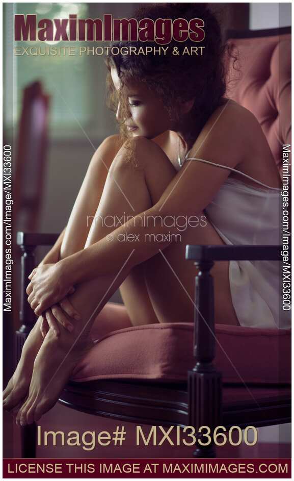 Sensual romantic portrait of young woman in night shirt sitting in armchair cuddled up