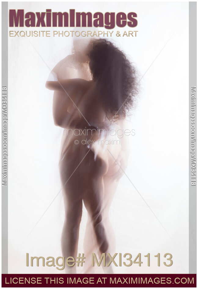 Sensual surreal photograph of a nude couple kissing in an embrace with their naked bodies behind sheer white veil