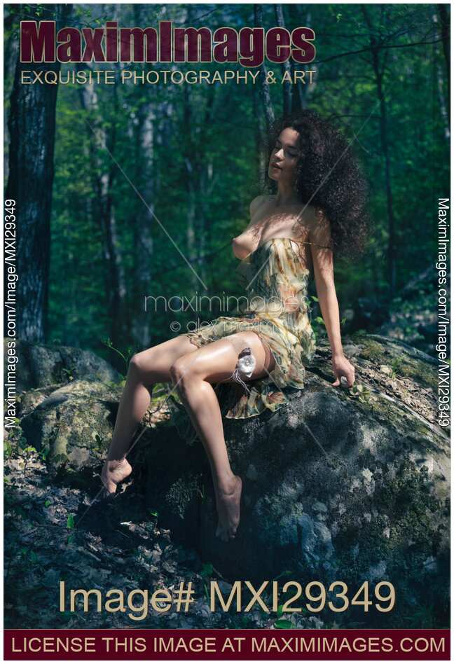Sensual young half nude woman sitting on a rock in a revealing summer dress