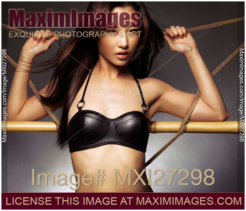 Sexy asian woman in black leather bra leaning against ropes