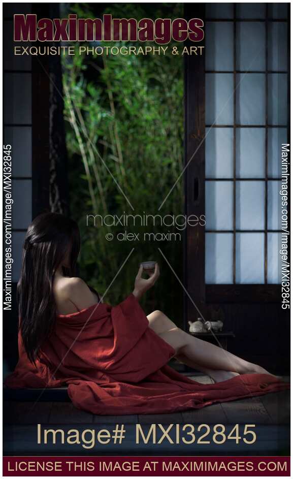 Sexy Asian woman in red kimono drinking tea half undressed by open shoji doors in historic Japanese house