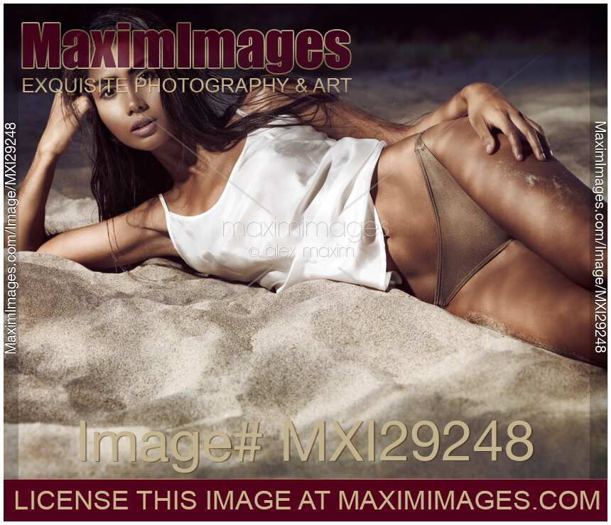 Sexy beautiful exotic woman lying on beach sand in dramatic light