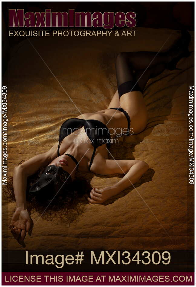 Sexy cat woman in black lingerie and stockings lying on bed in provocative seductive pose wearing kitty mask