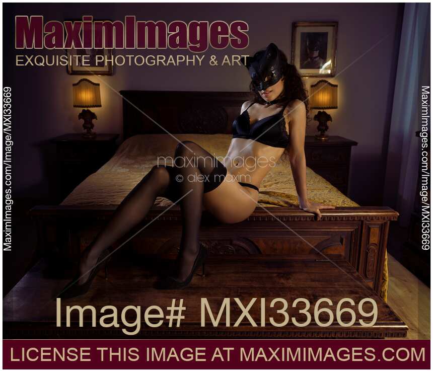 Sexy cat woman in black lingerie and stockings wearing a kitty mask reclining on antique bed with a provocative expression