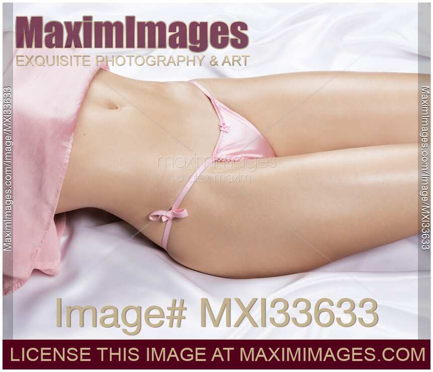 Sexy closeup of beautiful woman body with sensual curves and glowing skin in pink lingerie panties lying on white satin bed