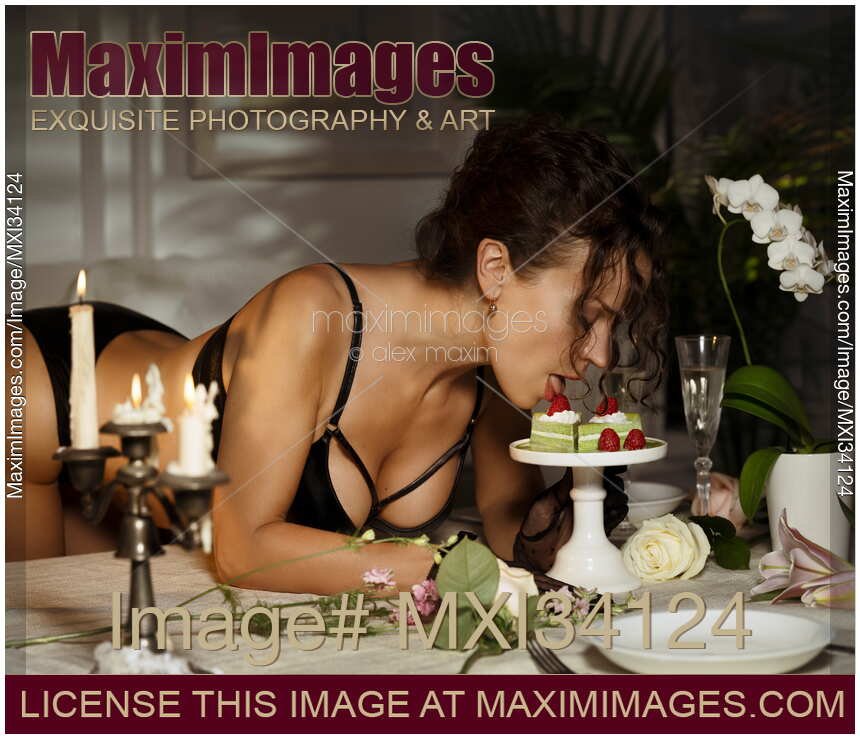Sexy glamorous woman in lingerie eating a dessert with her sensual mouth and tongue from a stand on a table