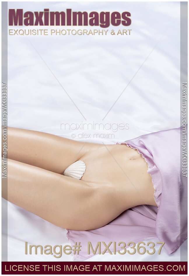 Sexy half-naked woman bared body midsection with sensual curves on white satin bed barely covered with a seashell