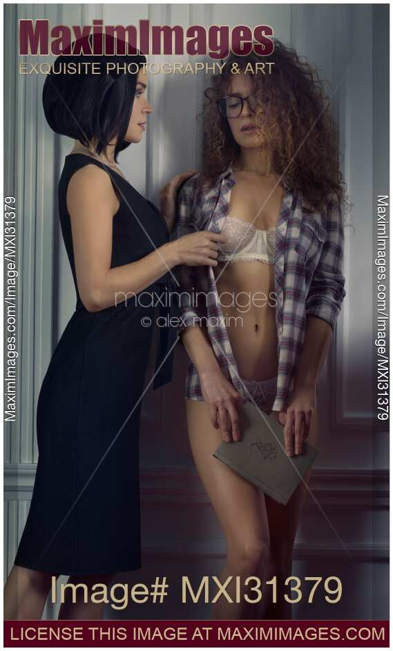 Sexy lesbian couple a woman undressing a shy girl in glasses leaning against a wall with a book