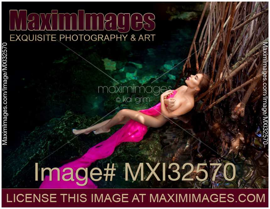 Sexy nude woman lying in clear water of a cenote covering her naked body with pink fabric