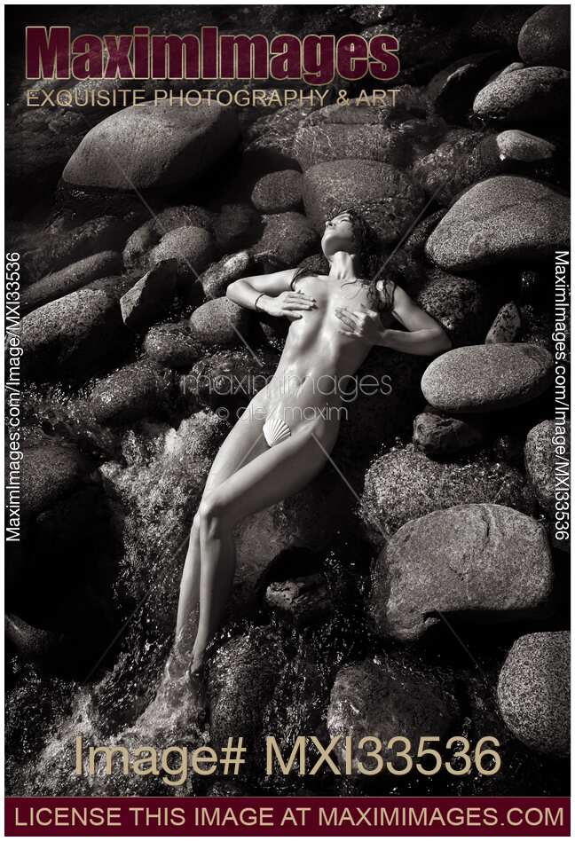 Sexy nude woman lying on rocks in water with her sensual wet naked body barely covered with sea shell Black and white