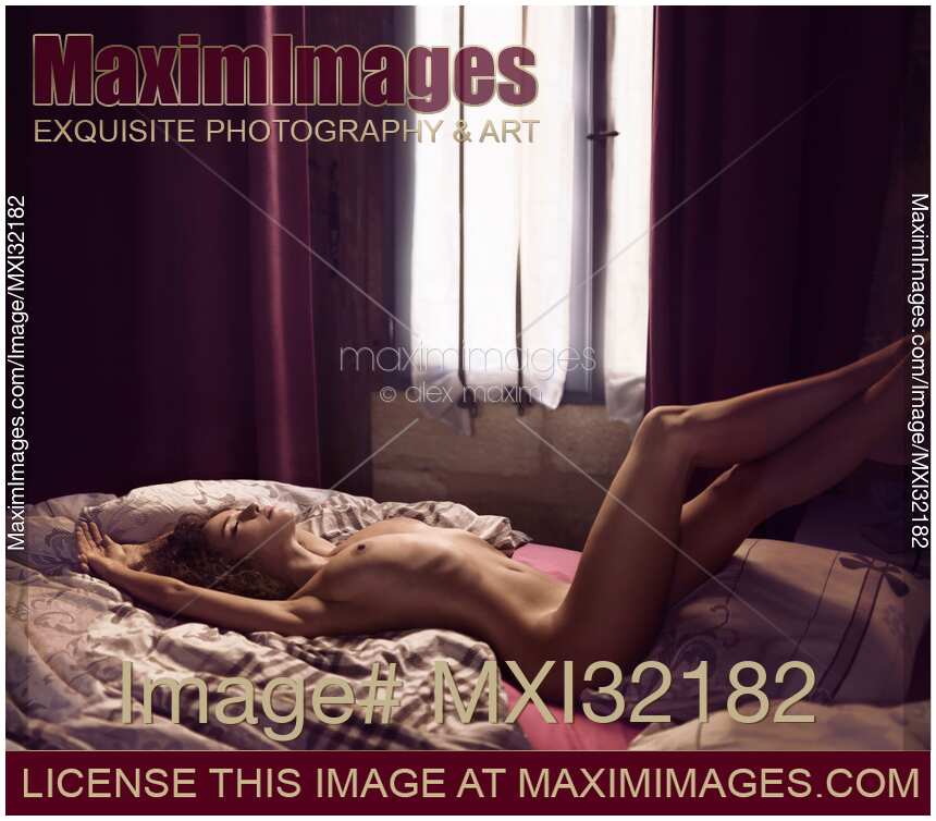 Sexy nude woman lying relaxed on a bed by a window with her legs on headboard