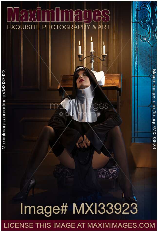 Sexy nun sitting in a provocative suggestive pose on praying bench with her legs in stockings spread wide apart