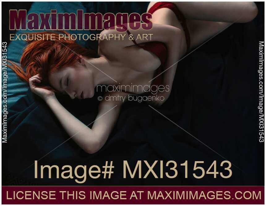 Sexy red haired woman in lingerie lying on a bed with closed eyes in a seductive pose