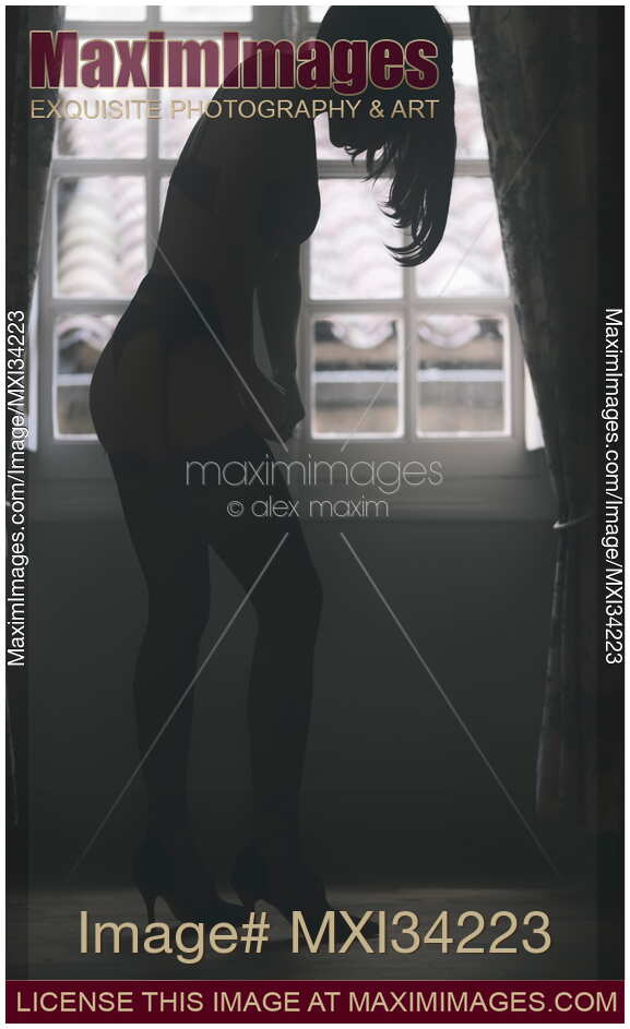 Sexy silhouette of a woman in lingerie putting on black stockings in a dark room by the window