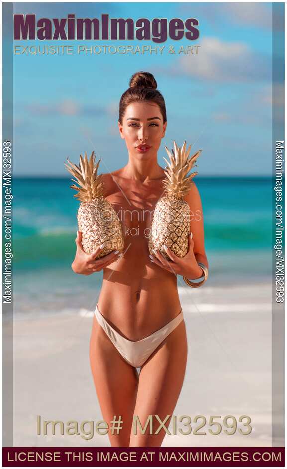 Sexy sun-tanned exotic woman topless at the beach covering her breasts with two pineapples Glamour portrait