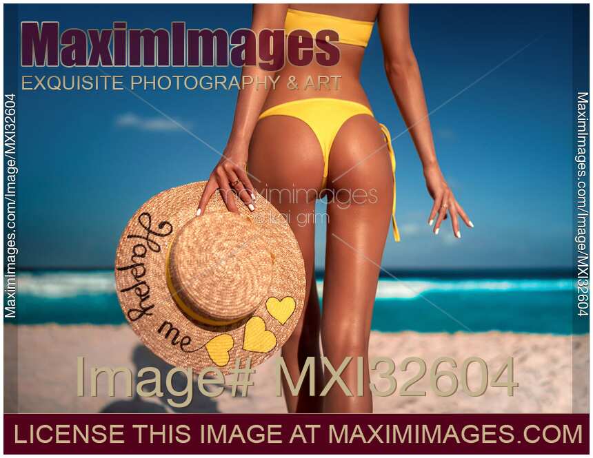Sexy sun-tanned woman in a bright swimsuit with a straw sun hat at a tropical beach closeup of her back and buttock