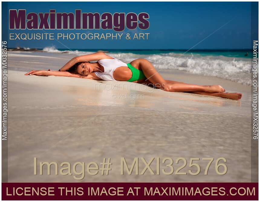 Sexy sun-tanned woman in a fashion bathing suit lying on white sandy shore of an ocean beach glamour portrait
