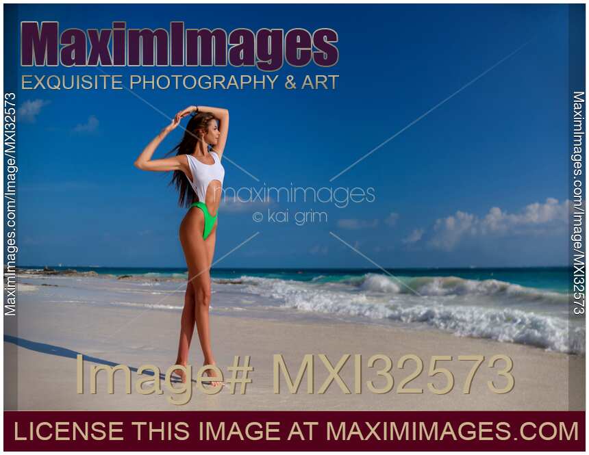 Sexy sun-tanned woman in fashion bathing suit on white sandy shore of an ocean beach
