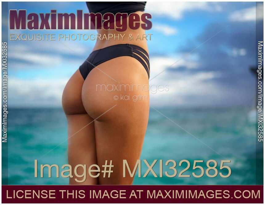 Sexy suntanned woman in bikini swimsuit closeup of midsection and buttocks over turquoise blue sea water
