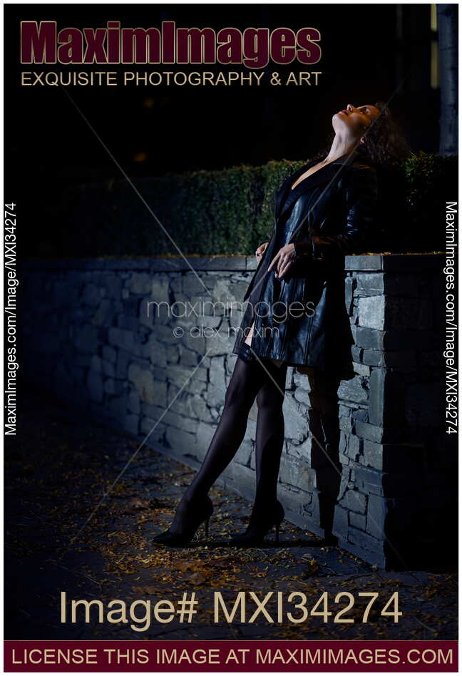 Sexy woman dressed in black leather coat and black stockings standing on city street looking at night sky