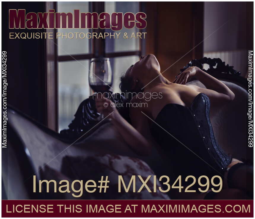 Sexy woman in black corset with a glass of wine leaning against backrest exposing her sensual neck and chest