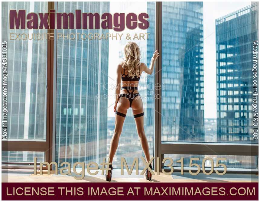 Sexy woman in black stripy underwear standing by a high-rise apartment window looking outside