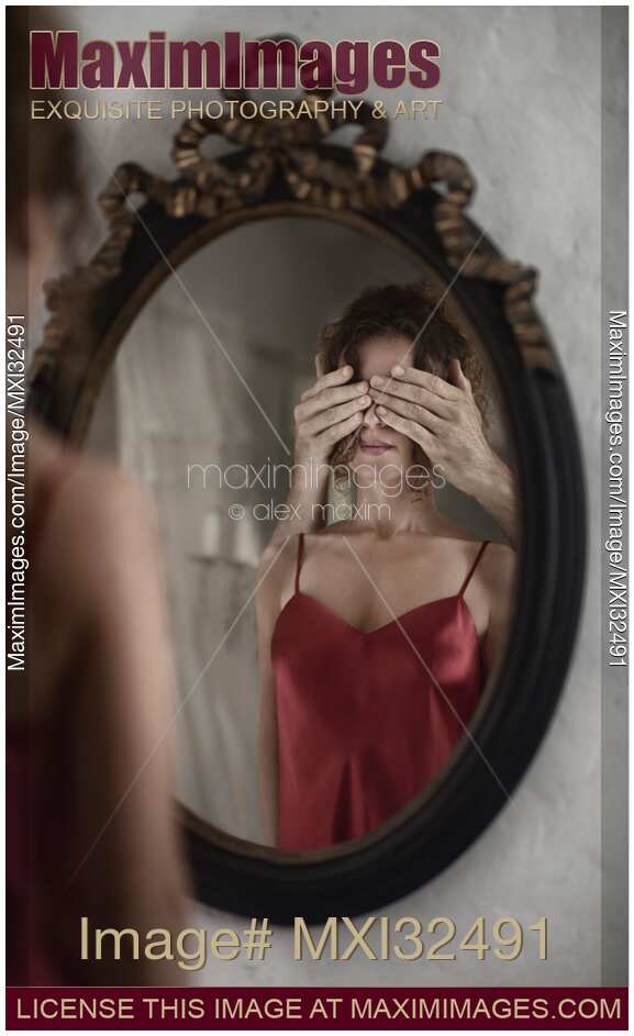 Sexy woman in red nightgown reflecting in a mirror with male hands covering her eyes from behind