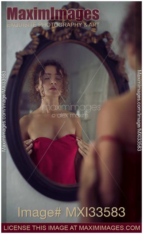 Sexy woman in red silky nightgown by the mirror with male hands undressing her from behind