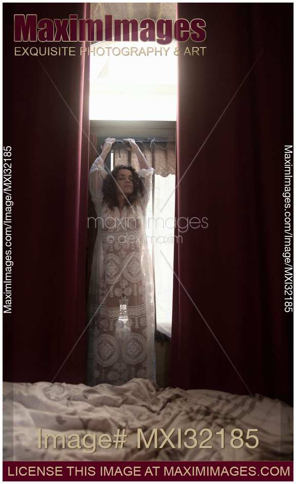 Sexy woman in see-through nightgown standing by the window in a seductive pose