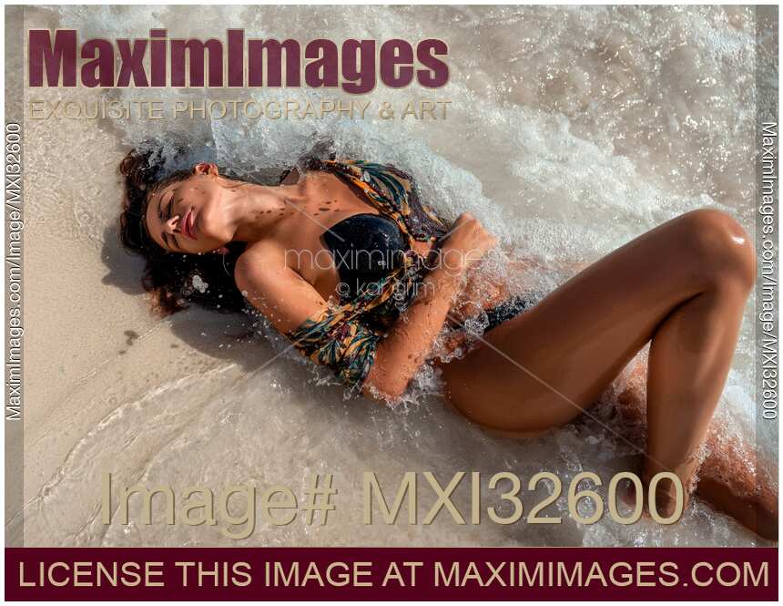 Sexy woman in swimsuit lying on a sandy shore with splashing waves of the Caribbean Sea hitting her body