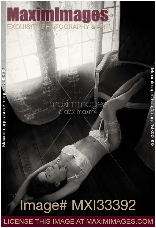 Sexy woman in white lingerie and stockings lying on the floor of a house by a sunlit window