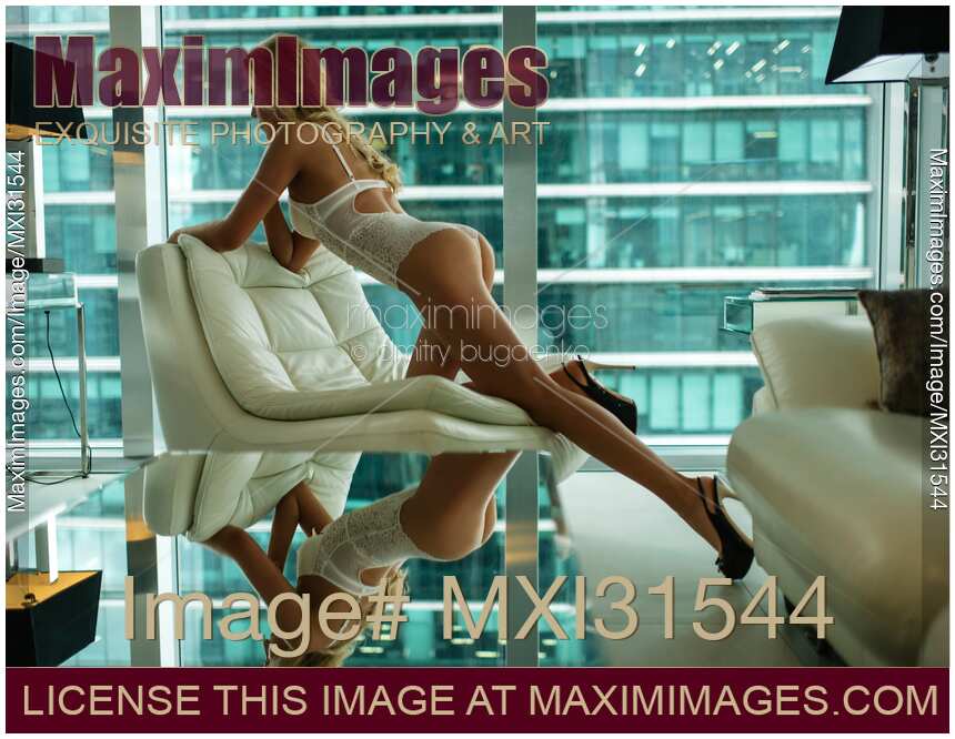 Sexy woman in white lingerie leaning on a chair by a window with office buildings view