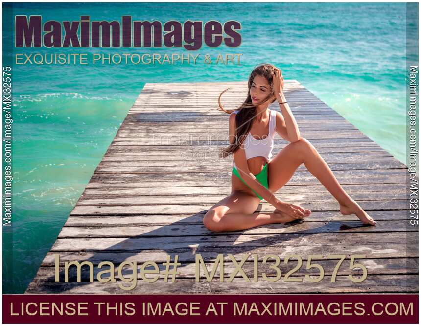 Sexy woman sitting on a pier in a one-piece swimsuit with turquoise sea water in the background