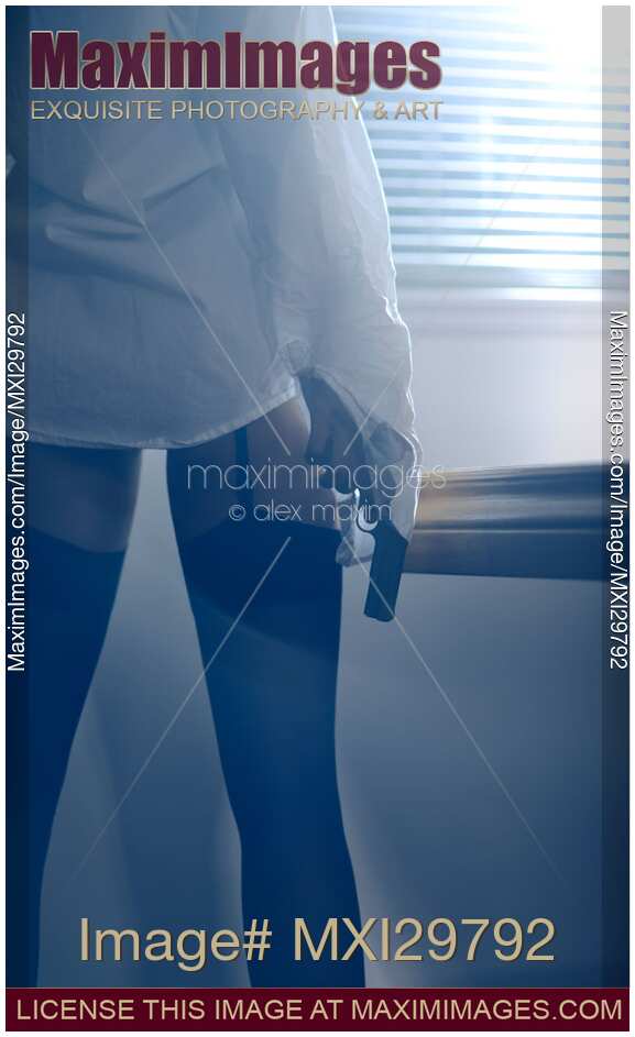 Sexy woman standing by the window with a gun in her hand wearing shirt and stockings