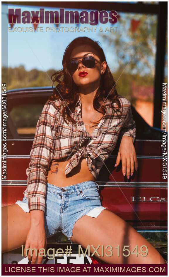 Sexy young woman in a shirt and shorts sitting on a bumper a retro car