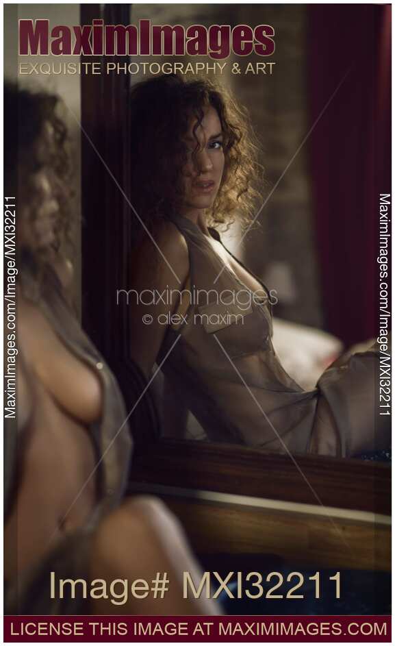 Sexy young woman in an unbuttoned dress sitting half undressed in front of a mirror with a seductive look