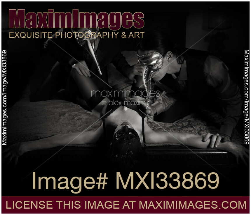 Sexy young woman in black underwear and mask bed making love with two gentlemen caressing her in bed. Sensual love threesome. Black and white.