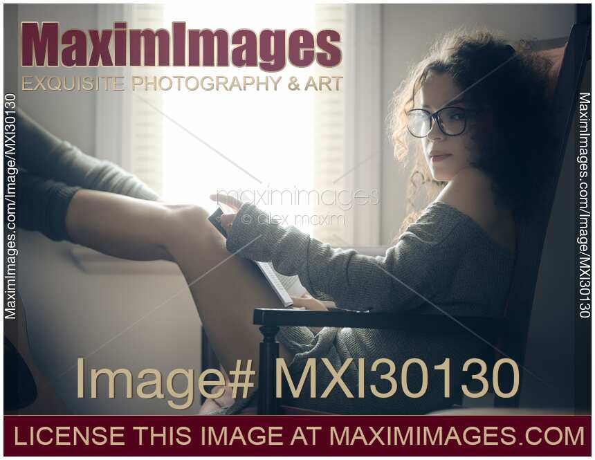 Sexy young woman in glasses sitting by the window with a book