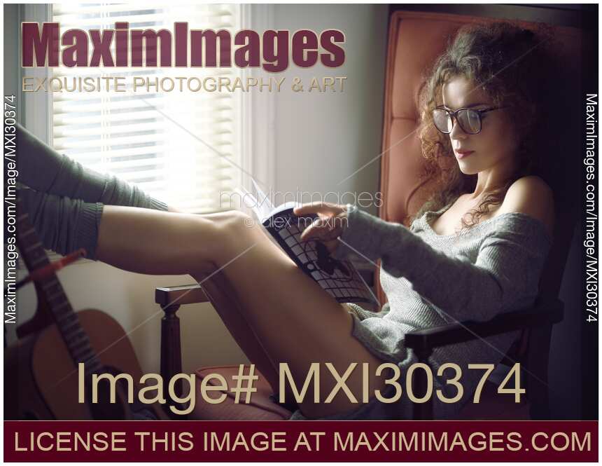Sexy young woman in large nerdy reading glasses with a book by a window