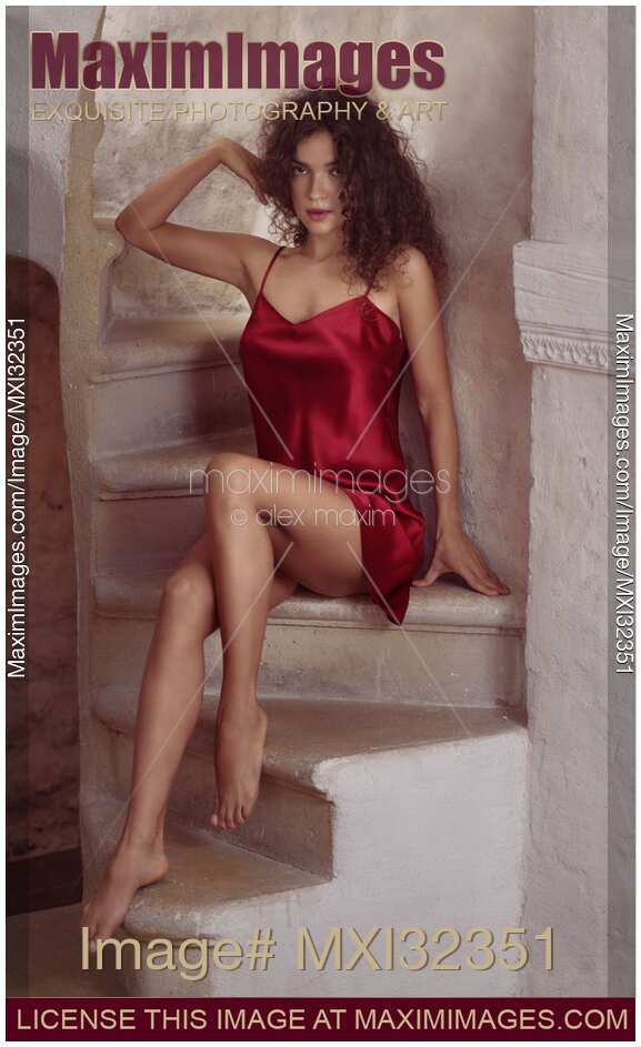 Sexy young woman in red silk nightgown sitting on a staircase of a French house with expressive look