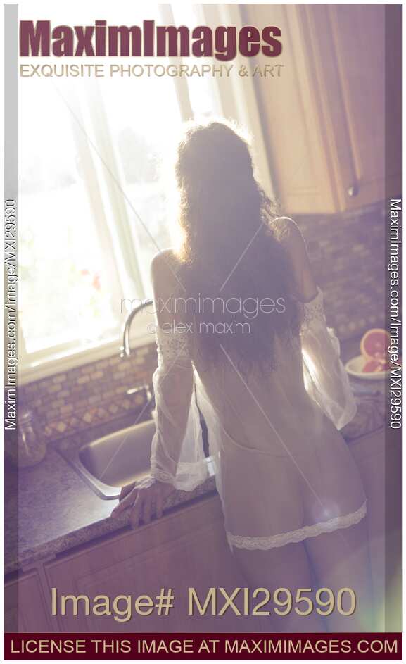 Sexy young woman in sheer night gown standing by a sun lit window in the morning