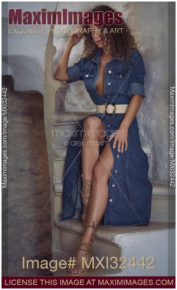 Sexy young woman in unbuttoned denim dress revealing her legs and cleavage sitting on a staircase of a French house